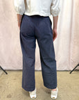 Person wearing navy pants and a white top against a plain background