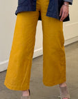 Woman wearing mustard yellow pants and a blue jacket indoors.