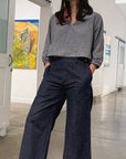 Woman standing in a modern art gallery wearing a gray top and dark blue pants.