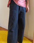Person wearing a gray shirt, pink top, and dark blue wide-leg pants on a yellow rug.
