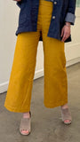 Woman wearing mustard yellow pants and a blue jacket indoors.